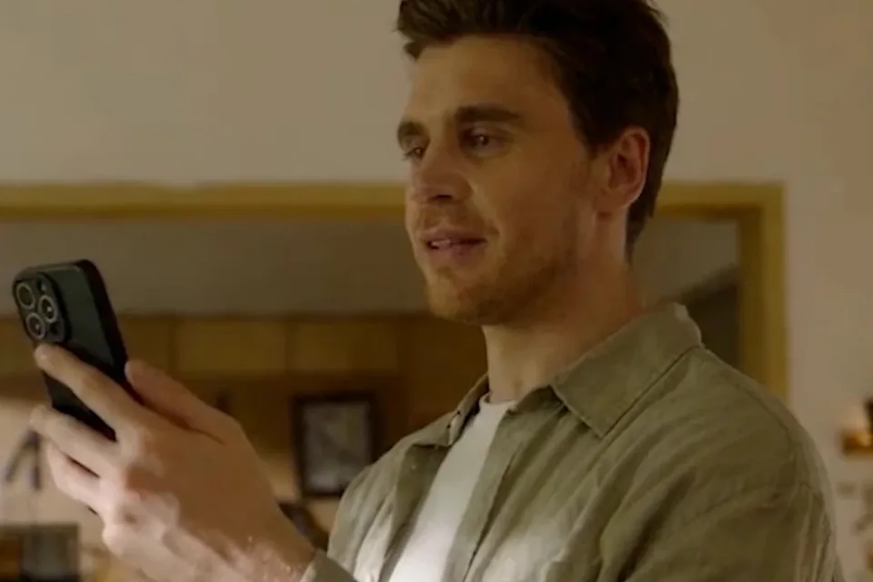 An adult son smiles while looking at his phone, as if reading an update from a parent’s home.