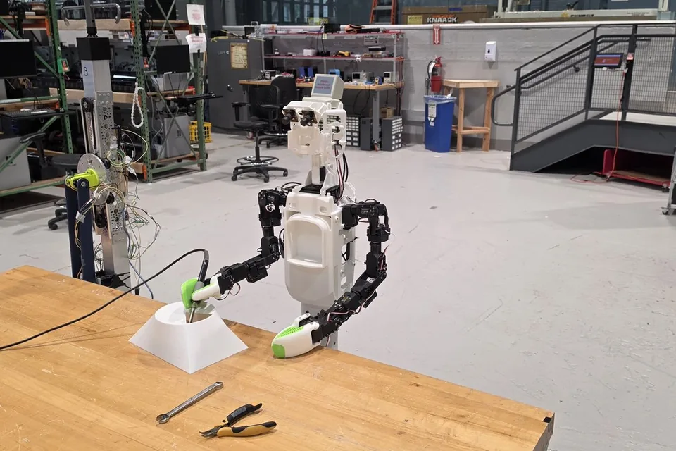 Robot arms and a KOKO prototype on workbenches in a Homebot One Inc lab.